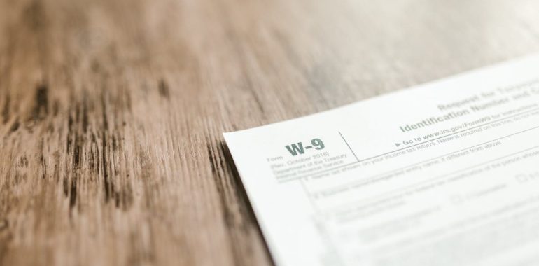 A close-up of a W-9 tax form placed on a wooden desk, emphasizing paperwork and finance.