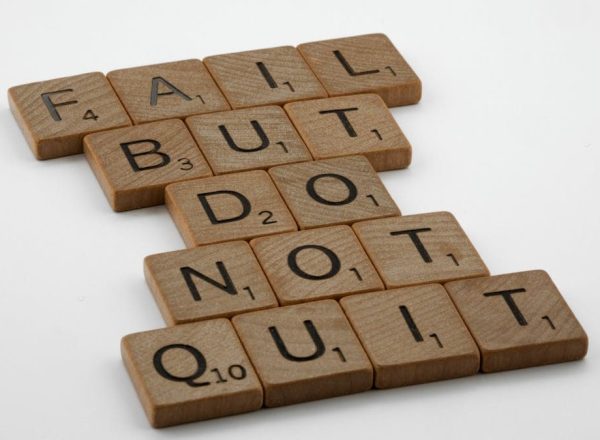 Close-up of Scrabble tiles forming the motivational phrase 'Fail but do not quit' on a white surface.