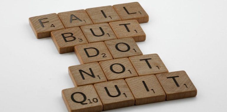 Close-up of Scrabble tiles forming the motivational phrase 'Fail but do not quit' on a white surface.