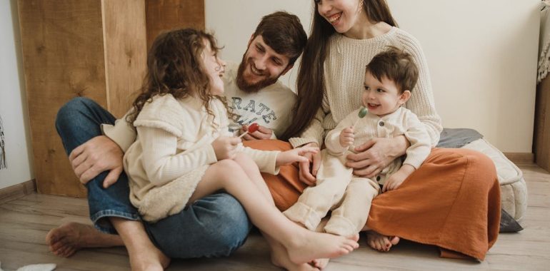 Smiling family of four sitting on the living room floor, enjoying quality time together.