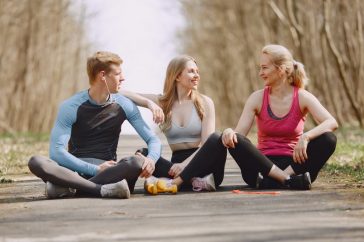 Three friends in sportswear sitting and conversing outdoors on a sunny day.
