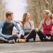 Three friends in sportswear sitting and conversing outdoors on a sunny day.