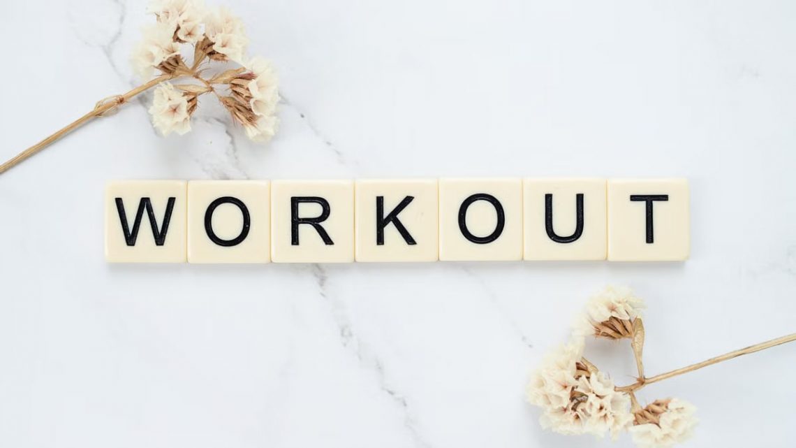 Letter tiles spelling 'WORKOUT' on marble with dried flowers, conveying fitness motivation.