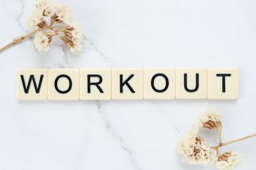 Letter tiles spelling 'WORKOUT' on marble with dried flowers, conveying fitness motivation.