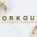 Letter tiles spelling 'WORKOUT' on marble with dried flowers, conveying fitness motivation.